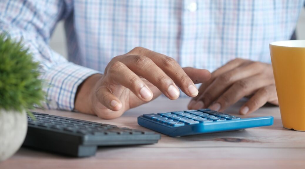 Hand bij een rekenmachine en laptop op een bureau