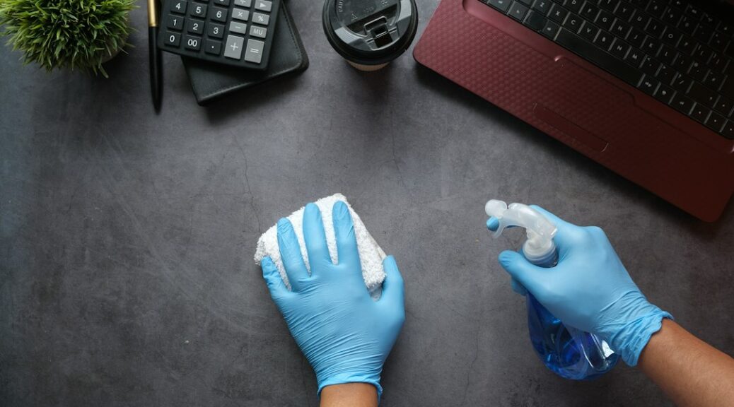 Handen met blauwe handschoenen reinigen een bureau met een doek en spray